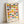 A framed poster featuring a geometric pattern of colorful circles arranged in horizontal rows. Each circle is divided in half with different color combinations including blues, greens, oranges, yellows, and pinks against a cream background. The design has a mid-century modern aesthetic with "BAUHAUS Est 1923" and "BAUHAUS AUSSTELLUNG WEIMAR | JULI 1923" text at the bottom. The poster is displayed in a light wood frame leaning against a white wall.