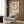 May include: Framed Bauhaus poster with colorful geometric circles in rows, displayed on wood paneled wall above beige upholstered chair with patterned pillow. Modern brass floor lamp and round black side table with open book nearby. Neutral tones with warm wood textures throughout contemporary living space.