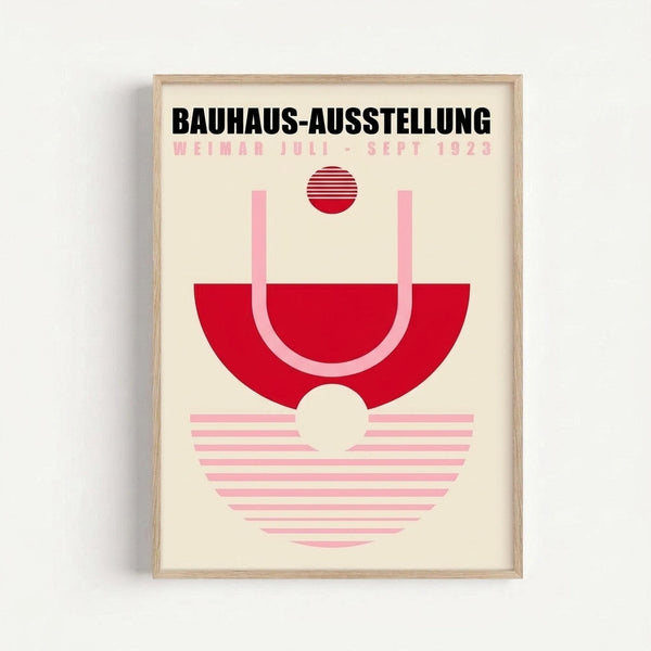 Framed vintage-style poster with cream background featuring bold black text "BAUHAUS-AUSSTELLUNG" and pink text "WEIMAR JULI-SEPT 1923". Abstract geometric design in red and pink tones shows circular and semi-circular shapes with horizontal striped patterns. Minimalist Bauhaus aesthetic with clean lines and modern typography, displayed in light wood frame against white wall.