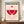 May include: Framed geometric poster with red and pink striped circular design on cream background, displayed on wooden sideboard next to white ceramic vase and stacked books in modern room with white paneled walls