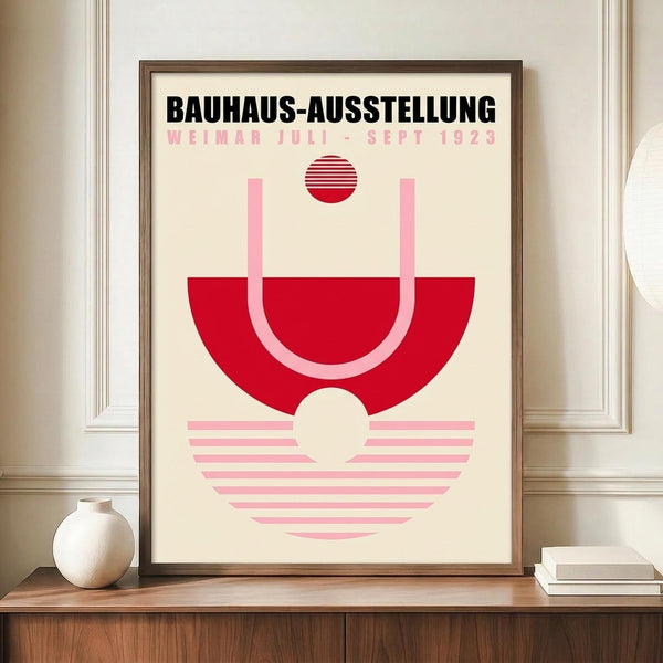 May include: Framed geometric poster with red and pink striped circular design on cream background, displayed on wooden sideboard next to white ceramic vase and stacked books in modern room with white paneled walls