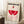 May include: Framed Bauhaus exhibition poster leaning against white wall corner, featuring geometric red and pink shapes with "BAUHAUS-AUSSTELLUNG WEIMAR JULI-SEPT 1923" text. Light wood frame, positioned on white textured rug next to wooden block with coffee cup, beige throw blanket draped nearby, soft natural lighting creating shadows.
