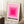 May include: A framed print featuring concentric pink squares in gradient shades from light to bright magenta, with black German text below reading "BAUHAUS-AUSSTELLUNG WEIMAR JULI - SEPT 1923". The wooden frame leans against white wainscoting beside a small wooden side table with white coffee cup and saucer, on a textured cream rug next to a beige knit throw blanket.