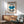 May include: Framed Bauhaus exhibition poster with geometric blue semicircle, black lines, striped patterns, and small circles on cream background. Displayed above wooden sideboard with ceramic lamp in modern living room setting with mint green mid-century armchair and round coffee table.
