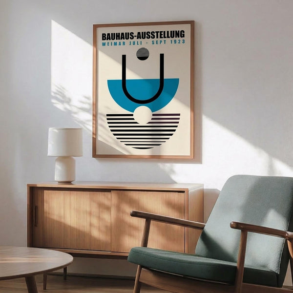May include: Framed Bauhaus exhibition poster with geometric blue semicircle, black lines, striped patterns, and small circles on cream background. Displayed above wooden sideboard with ceramic lamp in modern living room setting with mint green mid-century armchair and round coffee table.