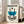 May include: Framed poster with cream background featuring geometric design in blue and black. Abstract composition shows curved and striped elements with small circles, displaying Bauhaus-style minimalist artwork. Light wood frame leans against white wall near beige upholstered chair in bright room with large windows.