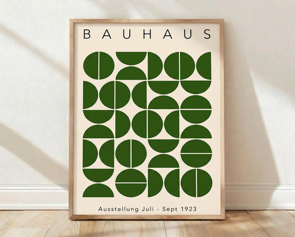 May include: Framed poster with cream background featuring green geometric circles and semicircles arranged in a grid pattern, displayed against white wall on wooden floor with natural lighting creating soft shadows. Light wood frame surrounds the minimalist Bauhaus-style design with black text at top and bottom.