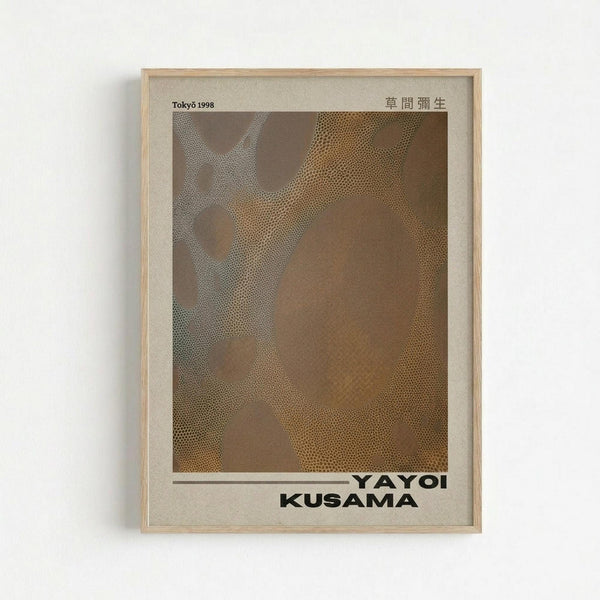 A framed poster featuring Yayoi Kusama's signature polka dot artwork in warm brown and golden tones. The abstract composition shows organic, flowing shapes covered in small dots against a brown background. The poster displays "Tokyo 1998" in the upper left corner, Japanese characters in the upper right, and "YAYOI KUSAMA" in bold black text at the bottom. The artwork is mounted in a light wood frame and hung on a white wall.