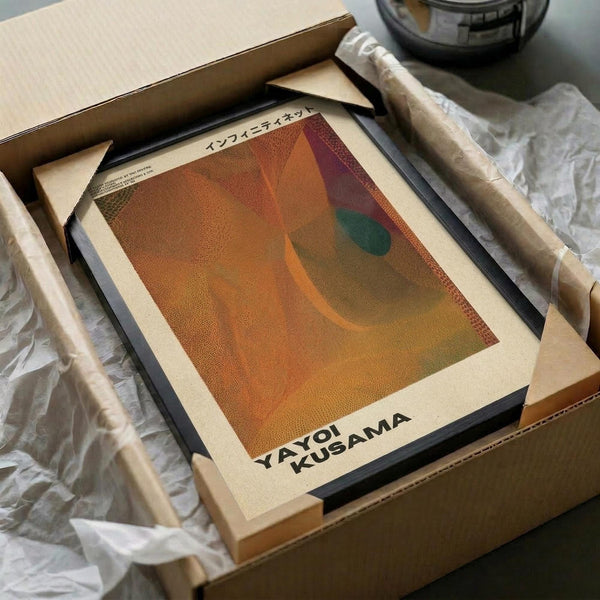 May include: Abstract art print with warm orange, brown and purple gradients and a small teal circle, displayed in black frame on cream mat. Print shows textured dotted pattern throughout. Packaged in brown cardboard box with white tissue paper on white surface alongside wooden dowels.