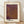 May include: Framed art print leaning against white wall on wooden floor. Light wood frame contains cream-colored poster with purple and brown textured pattern resembling organic cellular or net-like forms. Japanese text at top, "YAYOI KUSAMA" in bold black letters at bottom. Natural window light creates soft shadows on wall. Modern minimalist interior setting.