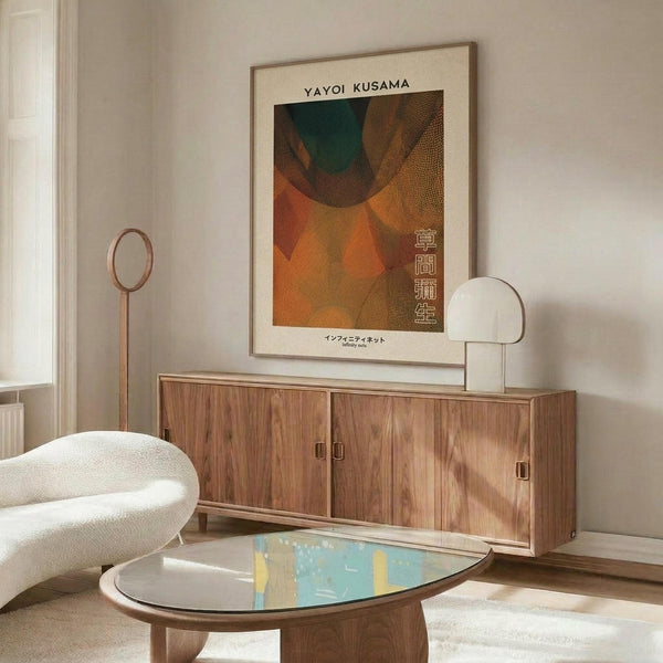 May include: Framed Yayoi Kusama exhibition poster with abstract orange, brown and teal organic shapes displayed above walnut credenza in modern living room. Poster features Japanese text and artist name. Room includes white curved chair, oval glass coffee table, brass floor lamp, and white table lamp on wooden sideboard.