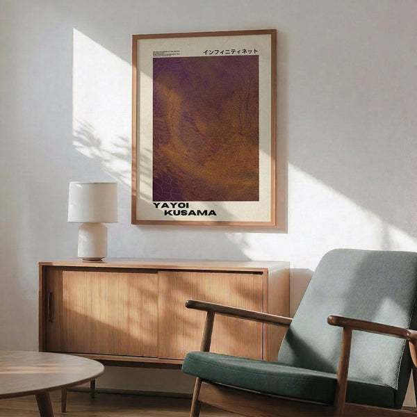 May include: Framed art print with purple and golden brown dotted pattern hanging above wooden sideboard. Mid-century modern interior with sage green armchair, white ceramic table lamp, and natural sunlight casting shadows on white wall. Warm wood tones throughout furniture pieces.