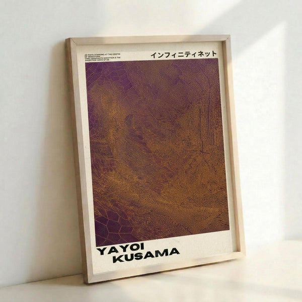 May include: Framed art print leaning against white wall showing abstract dotted pattern in purple and golden brown gradients. The artwork features Kusama's signature polka dot style with organic flowing forms. Text reads "YAYOI KUSAMA" at bottom and Japanese characters at top. Natural wood frame with white matting, photographed in bright indoor lighting that creates soft shadows on the wall.