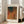 May include: Framed art print with abstract textured design in warm orange, brown, and teal tones featuring dotted patterns and organic shapes. White matted frame leans against white wall next to beige upholstered sofa in bright, minimalist living room with large windows and natural lighting on wooden floors.