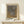 May include: Framed art print with abstract dotted pattern in gray and brown tones, displayed on light wood console table against cream wall. Small wrapped gift box with greenery sits nearby. Print features Japanese text at top and artist name at bottom in exhibition poster style with beige matting and thin wood frame.