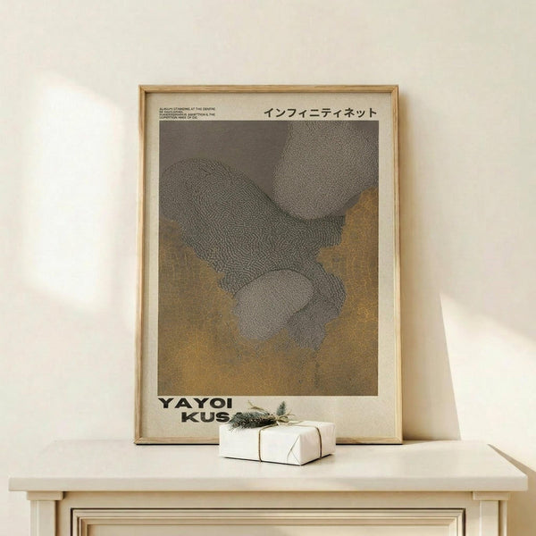 May include: Framed art print with abstract dotted pattern in gray and brown tones, displayed on light wood console table against cream wall. Small wrapped gift box with greenery sits nearby. Print features Japanese text at top and artist name at bottom in exhibition poster style with beige matting and thin wood frame.