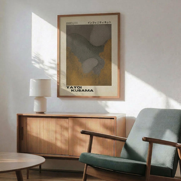 May include: Framed abstract art poster with organic dotted patterns in green, yellow and gray tones displayed above a wooden sideboard. Mid-century modern living room setting features a sage green armchair with wooden frame, white ceramic table lamp, and dramatic natural light casting shadows across white walls.