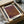 May include: Framed art print with purple and brown dotted pattern in minimalist style, displayed in wooden frame inside cardboard packaging with tissue paper and wooden dowels, sitting on white surface next to dark glass object