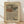 May include: Framed art print with flowing, wavy line patterns in earth tones of brown, beige, orange, and muted colors on textured beige background. Text reads "YAYOI KUSAMA" at top and Japanese character with "waves" at bottom. Light wooden frame sits on wooden floor against white wall with soft natural lighting and fabric shadows.