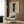 May include: Framed Yayoi Kusama-style poster with black and cream polka dot pattern creating an infinity net design, displayed above a beige armchair with geometric pillow in modern living room setting with wood paneled walls, gold floor lamp, and dark round side table with open book.
