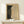 May include: Abstract art print in wooden frame showing black and cream halftone dot pattern creating curved, flowing forms. Japanese text visible at top. Print sits on light wood surface next to small wrapped white gift box with green sprig. Minimalist display against neutral wall with natural lighting.