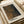 May include: Framed art print featuring a halftone dotted portrait in warm brown and orange tones with dark shadows, displayed on a light wooden surface alongside neutral-toned home decor items including a beige cylindrical object and dried plants