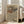May include: Large framed abstract poster with flowing wavy lines in earth tones of beige, brown, orange and muted colors, leaning against white wall next to beige upholstered chair in bright living room with tall windows and natural light casting shadows on wooden floor.