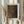 May include: Person holding framed poster print featuring abstract dotted pattern in earthy brown, orange and dark green tones, styled after Kusama's infinity net artwork. Light wood frame against neutral beige background with dried pampas grass stems. Japanese text visible at top of print.