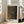 May include: Framed art print leaning against white wall next to beige upholstered chair in bright living room with large windows. Print features abstract dotted pattern in earth tones of brown, gold and dark green with Japanese text at top and "YAYOI KUSAMA" text at bottom. Natural wood frame with white matting, approximately 2-3 feet tall, positioned on light wooden floor.