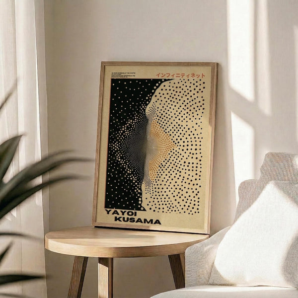 May include: Framed art print with black and cream polka dot pattern creating an infinity net design, displayed on a round wooden side table next to a beige upholstered chair. Natural sunlight streams across the neutral-toned room, casting soft shadows on the white walls. The artwork features dense dots transitioning from black to light areas, creating dimensional depth and movement within a thin wooden frame.