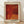 May include: Framed art print leaning against white wall on light wood floor. Poster features abstract red and orange dotted pattern with organic shapes and polka dot textures characteristic of contemporary Japanese art. Black text at bottom reads "YAYOI KUSAMA" with "Tokyo 1998" at top and Japanese characters in corner. Natural wood frame with cream matting, soft window light casting shadows across scene.