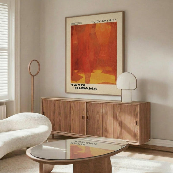 May include: Orange and red abstract dotted artwork with yellow elements hanging above wooden sideboard in modern living room. White curved chair and glass coffee table visible. Warm natural lighting creates shadows on cream walls. Contemporary interior styling with mid-century furniture pieces.