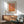 May include: Orange and pink abstract dotted artwork in wooden frame hanging on white wall above wooden sideboard. Modern living room setting with mint green upholstered chair, white table lamp, and round coffee table. Sunlight creates geometric shadows across the scene. Japanese text visible at top of framed print.