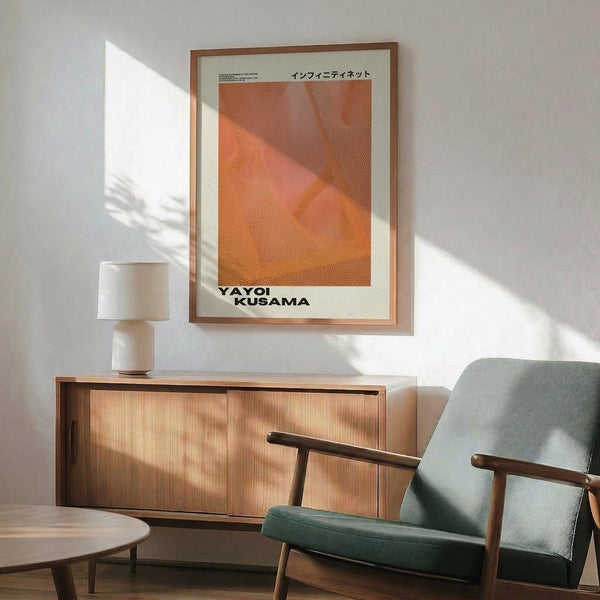 May include: Orange and pink abstract dotted artwork in wooden frame hanging on white wall above wooden sideboard. Modern living room setting with mint green upholstered chair, white table lamp, and round coffee table. Sunlight creates geometric shadows across the scene. Japanese text visible at top of framed print.