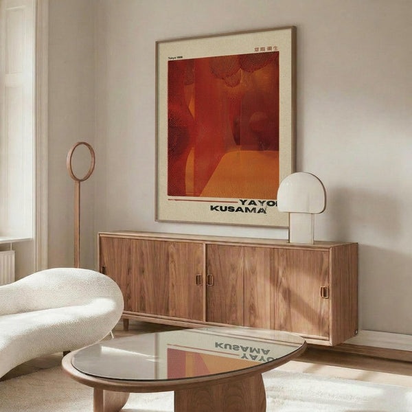 May include: Framed art print with abstract red and orange composition hanging above mid-century walnut credenza in minimalist living room. White upholstered chair and glass coffee table visible. Poster features geometric shapes in warm tones with Japanese text at top and artist name at bottom. Natural lighting creates shadows across polished wood surfaces.