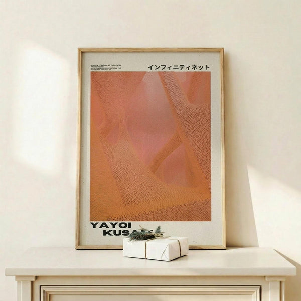 May include: Framed art print with orange abstract dotted pattern and Japanese text, displayed on light wood console table against cream wall. Small wrapped gift box with greenery sits beside the natural wood frame. Warm, minimalist home decor styling with soft natural lighting creating gentle shadows.