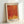 May include: Framed art print with orange and red abstract design featuring flowing dotted patterns and yellow geometric shapes at bottom, displayed in light wood frame against white wall. The poster shows textural halftone effects creating wave-like forms across the composition, with Japanese text at top and "YAYOI KUSAMA" text at bottom in bold black letters.