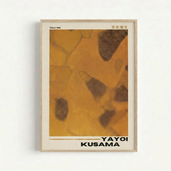 Framed exhibition poster featuring abstract orange and brown dotted pattern with organic curved shapes. The artwork uses halftone dot technique creating varying densities and shadows. Text reads "Tokyo 1998" at top with Japanese characters, and "YAYOI KUSAMA" in bold black letters at bottom. Light wood frame with white matting, displayed against cream colored wall.