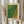May include: Person in cream ruffled blouse holding framed art print in light wooden frame. Print features green and orange gradient dotted pattern reminiscent of organic textures. Person also holds dried wheat or pampas grass stems. Soft natural lighting against neutral curtained background creates minimalist aesthetic.