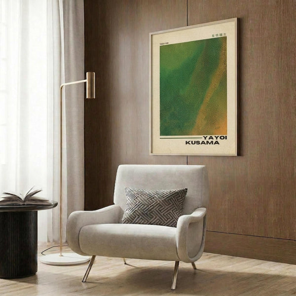 May include: Modern cream armchair with geometric throw pillow in contemporary living room setting with wood-paneled walls. Green and yellow abstract dotted art poster in light wooden frame hangs above chair. Gold floor lamp and dark side table with open book complete the minimalist interior design scene.