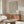 May include: Modern living room with warm wood credenza displaying framed poster featuring red-orange polka dot pattern creating optical illusion effect on cream background. Room includes curved white chair, glass-top coffee table, brass floor lamp, and table lamp in minimalist Scandinavian style interior with beige walls.