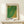 May include: Framed art print with green and yellow dotted pattern in natural wood frame, displayed on light wooden shelf against cream wall. Small wrapped gift box with sprig of greenery sits beside the frame. Print features Japanese text at top and artist name at bottom in bold black letters.