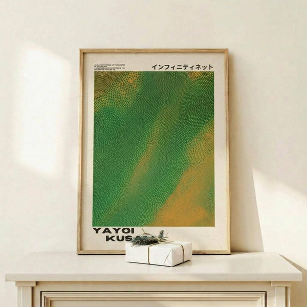 May include: Framed art print with green and yellow dotted pattern in natural wood frame, displayed on light wooden shelf against cream wall. Small wrapped gift box with sprig of greenery sits beside the frame. Print features Japanese text at top and artist name at bottom in bold black letters.