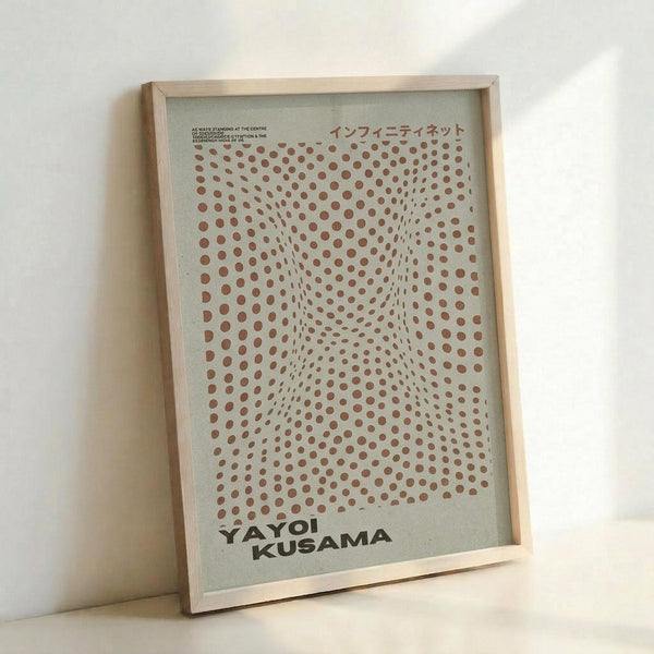 A framed poster with reddish-brown polka dots arranged in a warped grid pattern that creates an optical illusion of depth and movement on a light background. The artwork features Japanese text at the top and "YAYOI KUSAMA" in bold black letters at the bottom. The poster is displayed in a light wooden frame, leaning against a white wall.