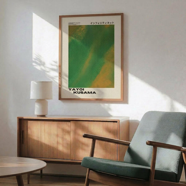 May include: Framed poster with green and yellow dotted pattern artwork hanging above wooden sideboard in modern living room. Mid-century furniture includes teal upholstered chair with wood arms, round coffee table, and credenza with sliding doors. White table lamp and natural sunlight create warm atmosphere on white walls.