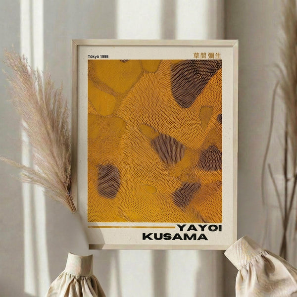 May include: Framed poster with yellow and orange abstract dotted pattern artwork in light wood frame, displayed on neutral wall beside dried pampas grass and beige fabric items with natural lighting creating soft shadows