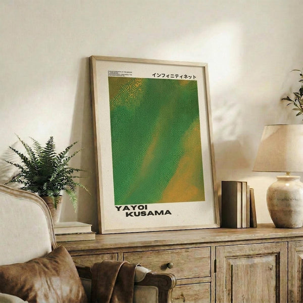 May include: Framed poster with green and yellow dotted pattern displayed on wooden sideboard alongside fern plant, books, and ceramic vase in modern living room with beige armchair and neutral walls
