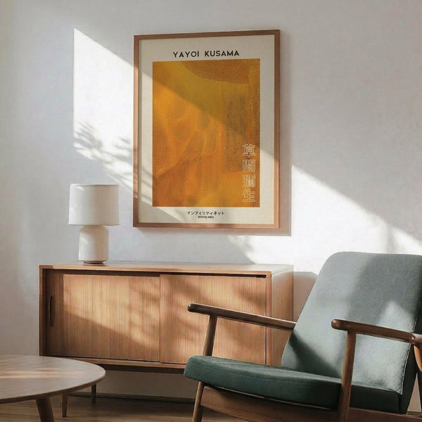 May include: Framed Yayoi Kusama Infinity Nets art print in warm golden orange tones with Japanese text, displayed above a mid-century modern wood credenza with white ceramic lamp. Mint green upholstered armchair with wooden frame sits beside round wood coffee table. Bright natural sunlight creates geometric shadows across white wall in minimalist living room setting.