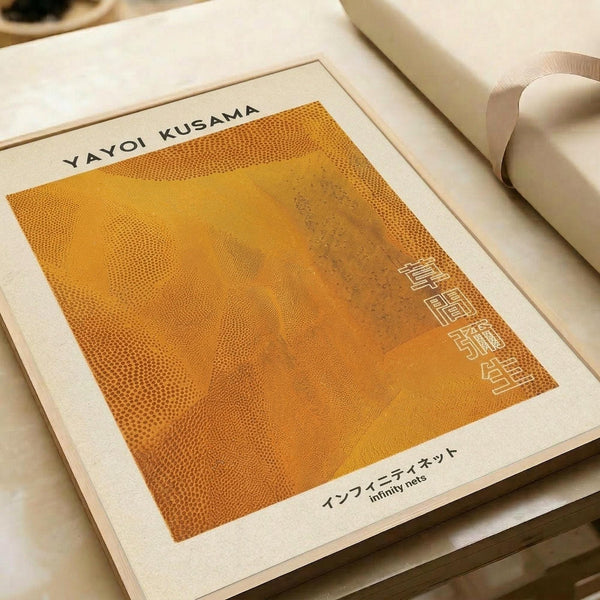 Minimalist art print with vibrant orange background and dotted pattern texture. The square composition features subtle geometric elements and Japanese text at the bottom reading "infinity nets." The print is displayed on cream-colored paper with clean white borders, photographed at an angle on a light wooden surface with rolled paper tubes visible in the background.