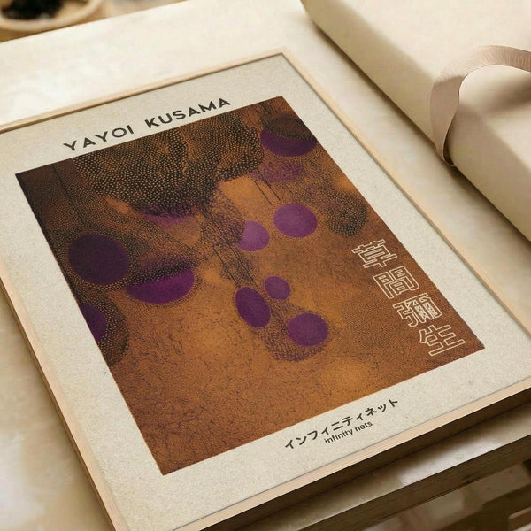 Print featuring abstract artwork with purple circular dots scattered across a textured orange-brown background with dotted patterns. The artist name "YAYOI KUSAMA" appears at top, with Japanese characters and "infinity nets" text at bottom. White matted border surrounds the artwork, displayed on neutral paper surfaces with soft lighting.